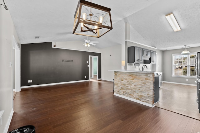 kitchen with a textured ceiling, lofted ceiling, a sink, light countertops, and dark wood-style floors