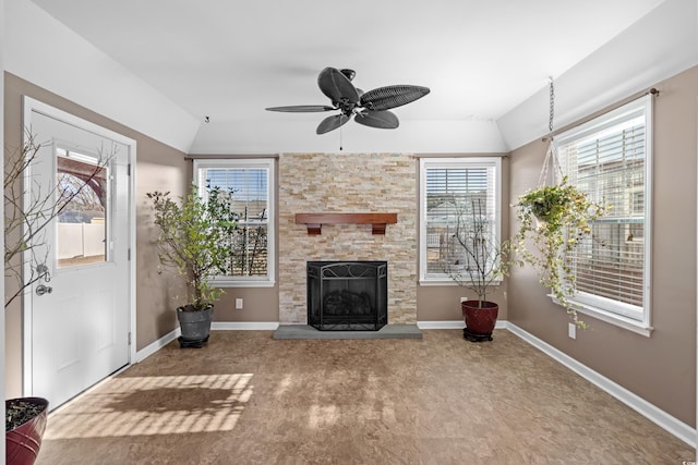 unfurnished living room featuring ceiling fan, baseboards, and a stone fireplace