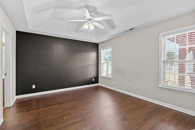 unfurnished room with baseboards, visible vents, a raised ceiling, and dark wood finished floors