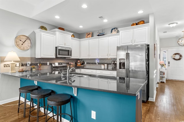 kitchen with stainless steel appliances, kitchen peninsula, a breakfast bar area, white cabinets, and dark wood-type flooring