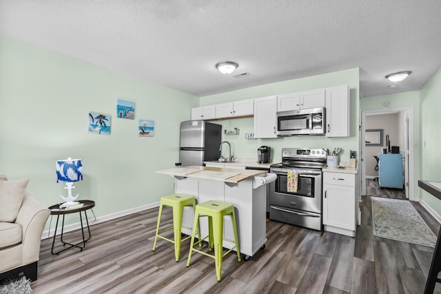 kitchen with white cabinets, stainless steel appliances, dark hardwood / wood-style floors, and a breakfast bar area