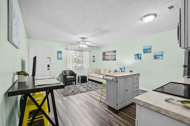 interior space with a textured ceiling, a kitchen bar, gray cabinets, dark hardwood / wood-style flooring, and ceiling fan