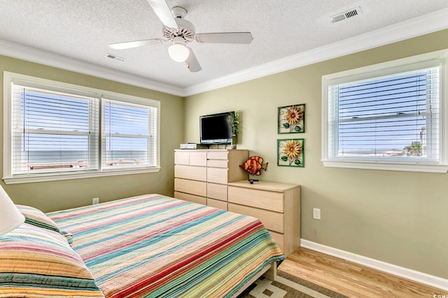 bedroom featuring a textured ceiling, light wood-type flooring, ornamental molding, and ceiling fan