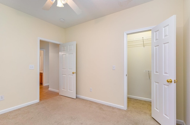 unfurnished bedroom featuring ceiling fan, light carpet, a closet, and a walk in closet