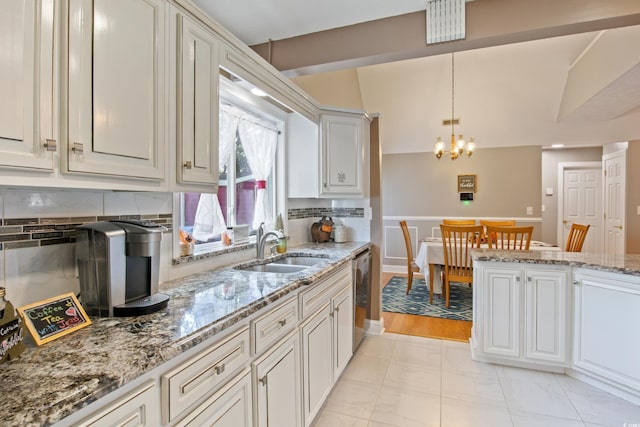 kitchen with sink, an inviting chandelier, light stone counters, hanging light fixtures, and stainless steel dishwasher