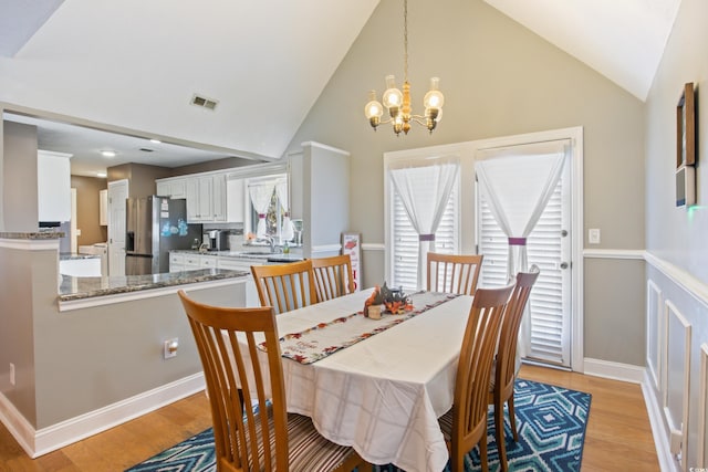 dining room featuring vaulted ceiling, sink, a chandelier, and light wood-type flooring