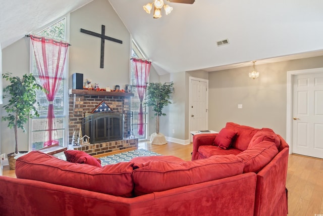 living room featuring lofted ceiling, a brick fireplace, ceiling fan with notable chandelier, and wood-type flooring