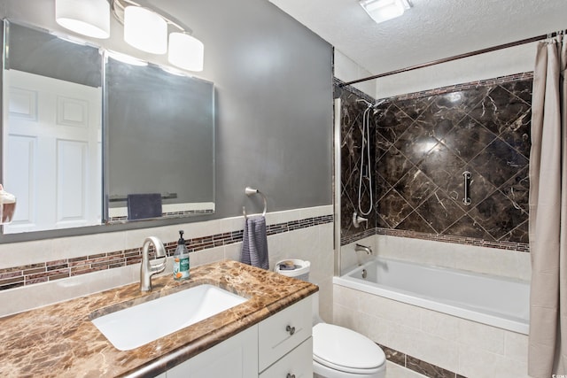 full bathroom featuring shower / tub combo with curtain, tile walls, vanity, toilet, and a textured ceiling