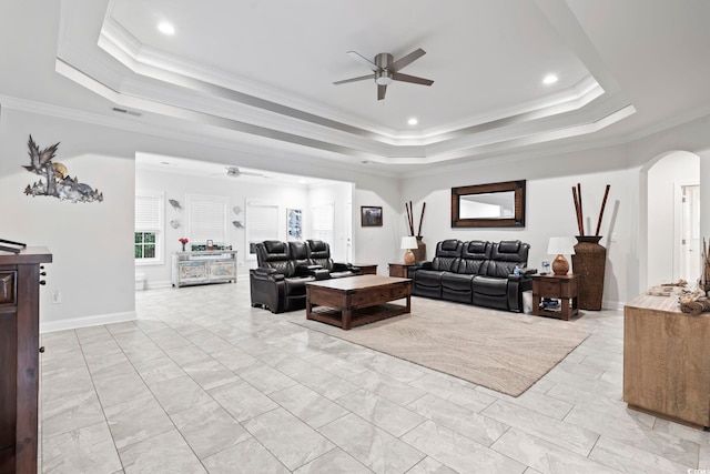 living room with arched walkways, a tray ceiling, and ornamental molding