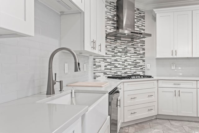 kitchen with a sink, backsplash, light countertops, and wall chimney range hood