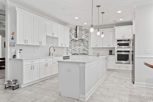 kitchen featuring wall chimney range hood, a center island with sink, light countertops, stainless steel double oven, and white cabinetry