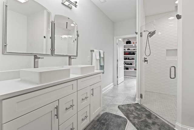 bathroom with a walk in closet, a shower stall, double vanity, and a sink