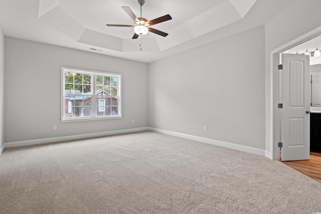 empty room featuring visible vents, carpet, baseboards, a raised ceiling, and a ceiling fan