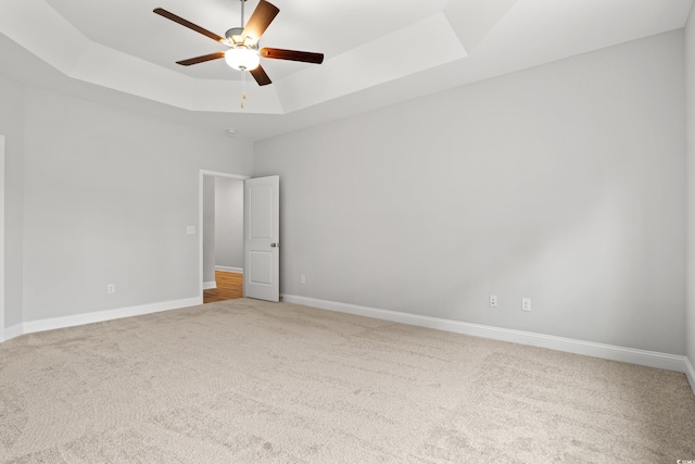 unfurnished room with a raised ceiling, baseboards, carpet floors, and ceiling fan