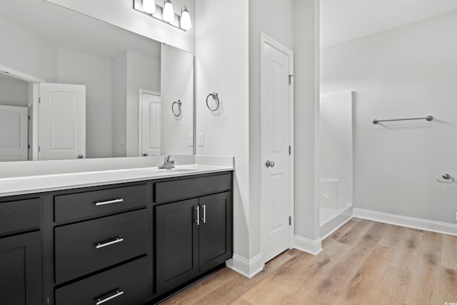 bathroom with vanity, a shower, baseboards, and wood finished floors