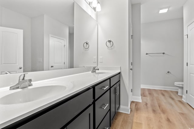 bathroom featuring double vanity, toilet, wood finished floors, and a sink