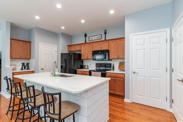 kitchen featuring black appliances, light hardwood / wood-style floors, a kitchen island with sink, and a breakfast bar area