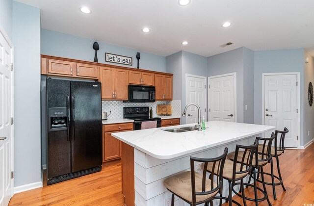 kitchen with a breakfast bar, black appliances, sink, an island with sink, and light hardwood / wood-style floors