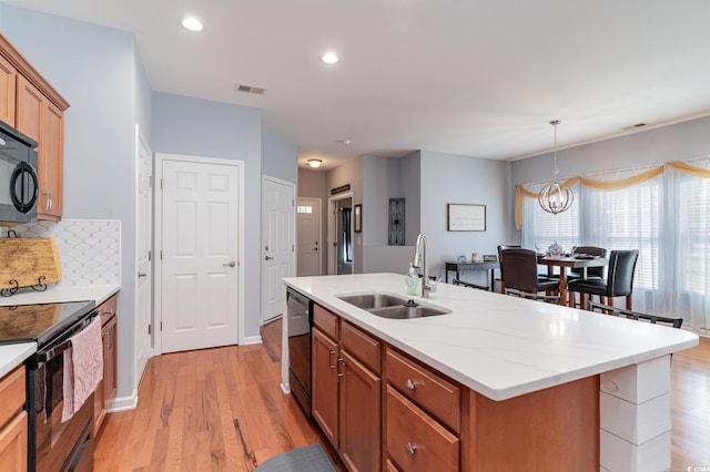 kitchen with light wood-type flooring, backsplash, black appliances, sink, and an island with sink