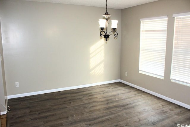 empty room with dark wood-type flooring, a textured ceiling, and an inviting chandelier