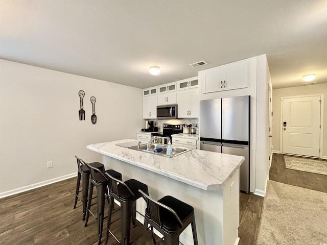 kitchen with a breakfast bar, a kitchen island with sink, light stone countertops, appliances with stainless steel finishes, and white cabinetry