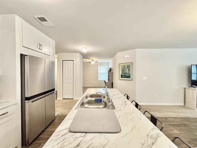 kitchen with white cabinetry, stainless steel fridge, sink, and light stone counters