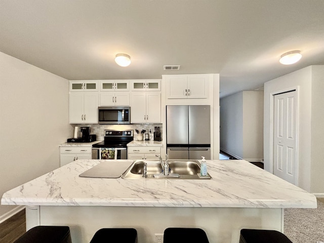 kitchen featuring a breakfast bar, white cabinets, a center island with sink, and appliances with stainless steel finishes