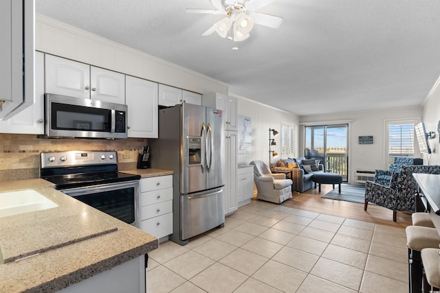 kitchen with stainless steel appliances, white cabinets, light tile patterned floors, ornamental molding, and ceiling fan