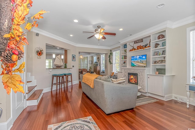 living area featuring crown molding, wood finished floors, ceiling fan, and a glass covered fireplace