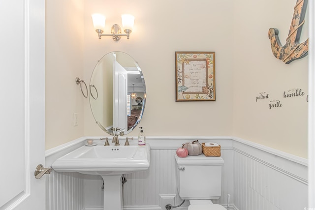 half bathroom featuring a sink, toilet, and wainscoting