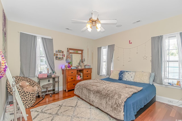 bedroom featuring ceiling fan, visible vents, baseboards, and wood finished floors