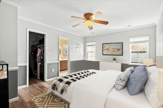 bedroom featuring ensuite bathroom, a walk in closet, ceiling fan, ornamental molding, and a closet