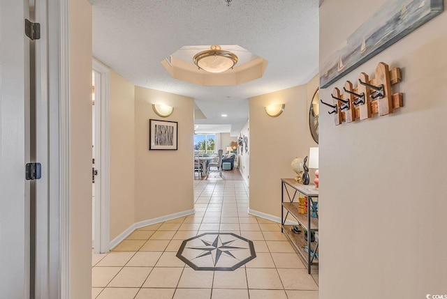 hall featuring a textured ceiling, light tile patterned flooring, and a raised ceiling