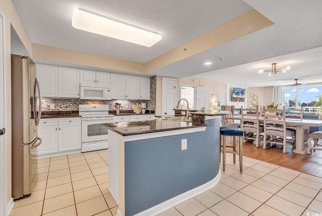 kitchen with a center island with sink, a textured ceiling, sink, a breakfast bar area, and white appliances