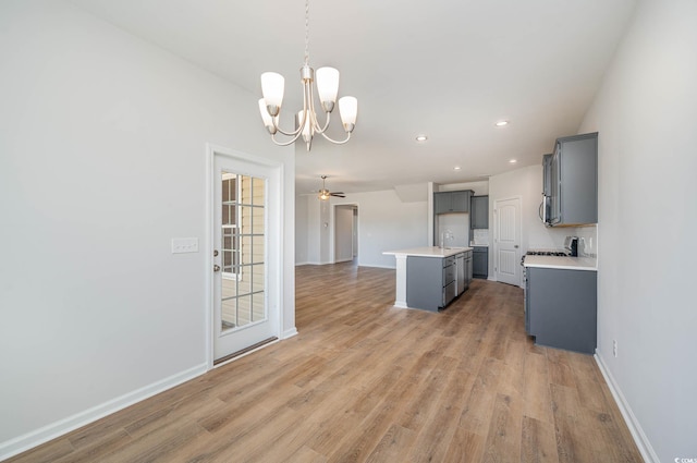 kitchen with an island with sink, hanging light fixtures, gray cabinetry, and light wood-type flooring