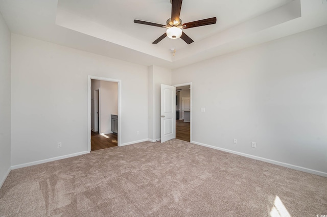 unfurnished bedroom featuring dark colored carpet, ceiling fan, and a tray ceiling