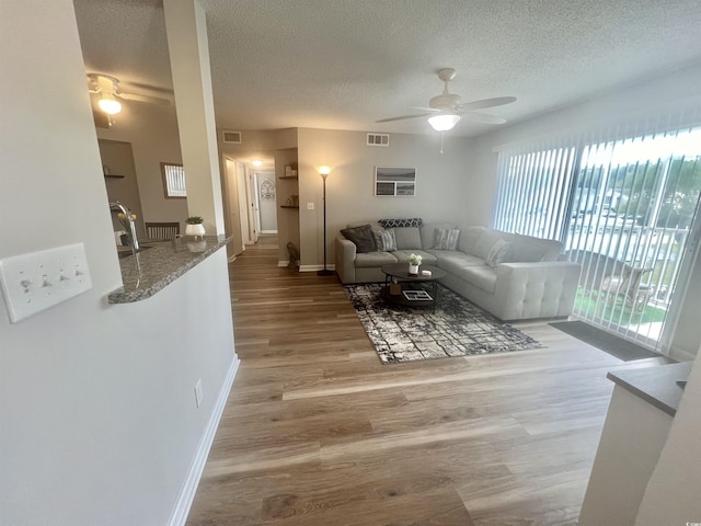 living room featuring ceiling fan, a textured ceiling, and light hardwood / wood-style floors