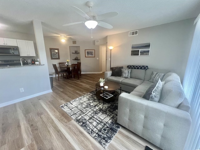 living room with a textured ceiling, light hardwood / wood-style flooring, and ceiling fan