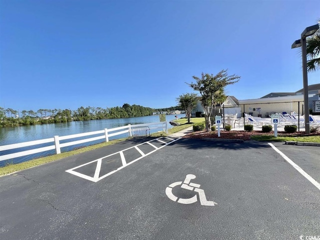 uncovered parking lot with a water view and fence