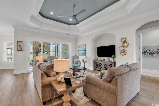 living room with ceiling fan, a raised ceiling, ornamental molding, and plenty of natural light