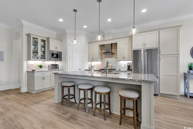 kitchen featuring decorative light fixtures, tasteful backsplash, wall chimney range hood, an island with sink, and stainless steel appliances