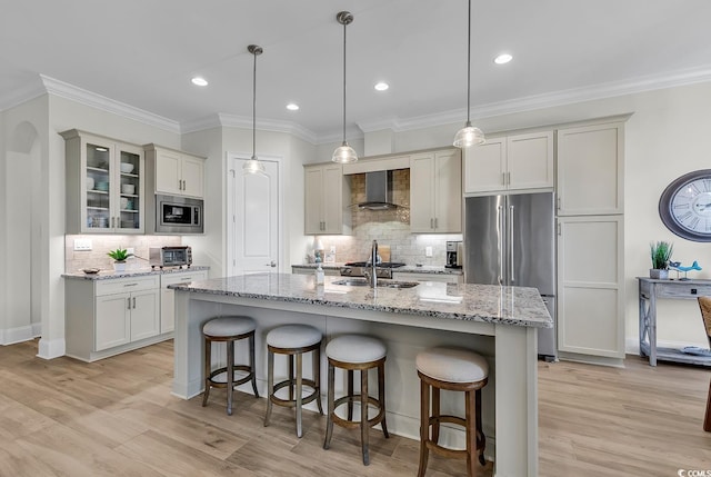 kitchen featuring appliances with stainless steel finishes, decorative light fixtures, wall chimney exhaust hood, light stone counters, and a center island with sink