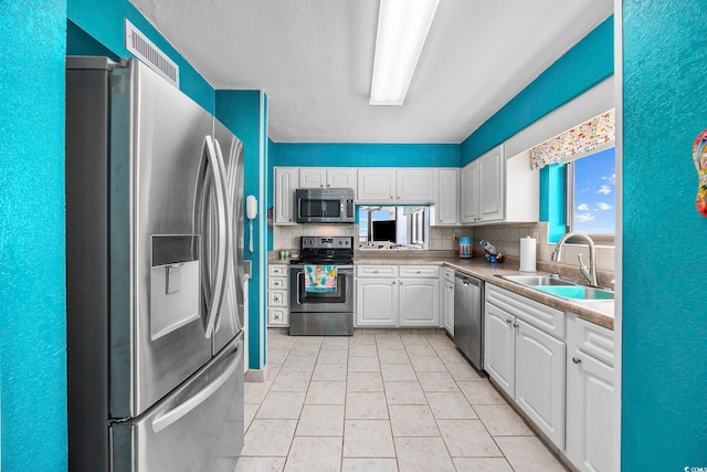 kitchen with sink, stainless steel appliances, light tile patterned floors, tasteful backsplash, and white cabinets