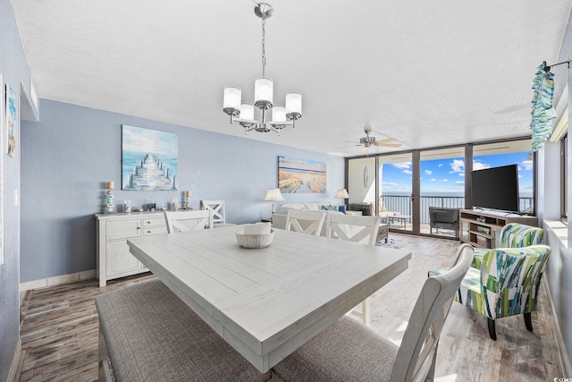 dining area with ceiling fan with notable chandelier, a textured ceiling, light wood-type flooring, and floor to ceiling windows