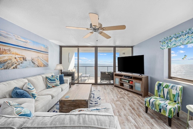 living room with ceiling fan, expansive windows, a textured ceiling, and light wood-type flooring