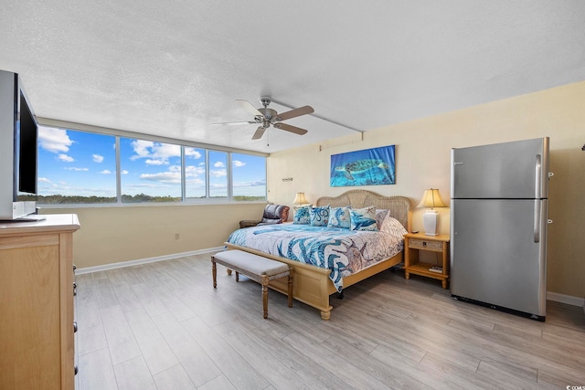 bedroom featuring stainless steel refrigerator, ceiling fan, light hardwood / wood-style floors, and a textured ceiling