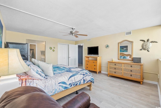 bedroom with stainless steel fridge, a textured ceiling, light hardwood / wood-style floors, and ceiling fan