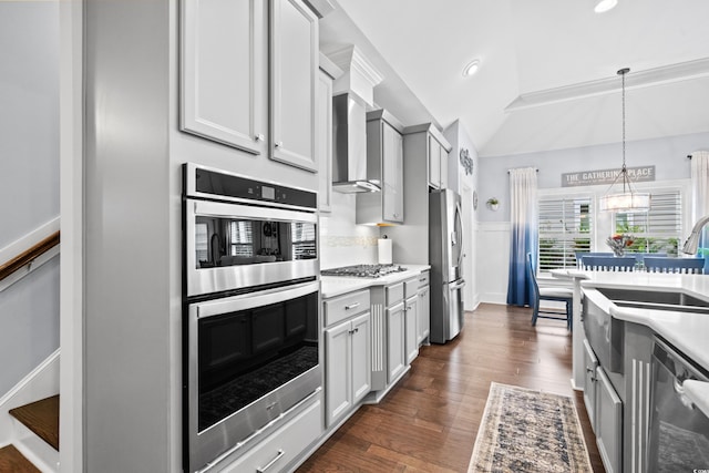 kitchen with appliances with stainless steel finishes, hanging light fixtures, a notable chandelier, dark wood-type flooring, and wall chimney range hood