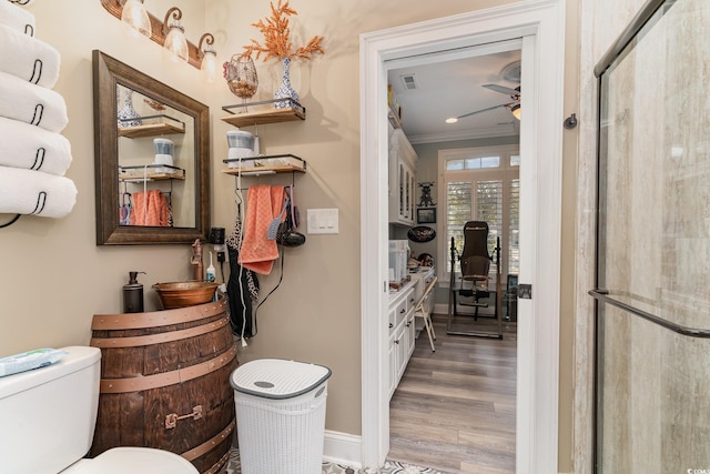 bathroom with wood-type flooring, a shower with door, ornamental molding, toilet, and ceiling fan