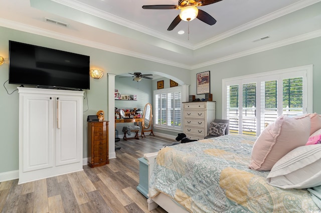 bedroom with ceiling fan, a raised ceiling, light wood-type flooring, and crown molding